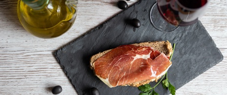 Detalle de tapa de jamón con aceite y copa de vino tinto 